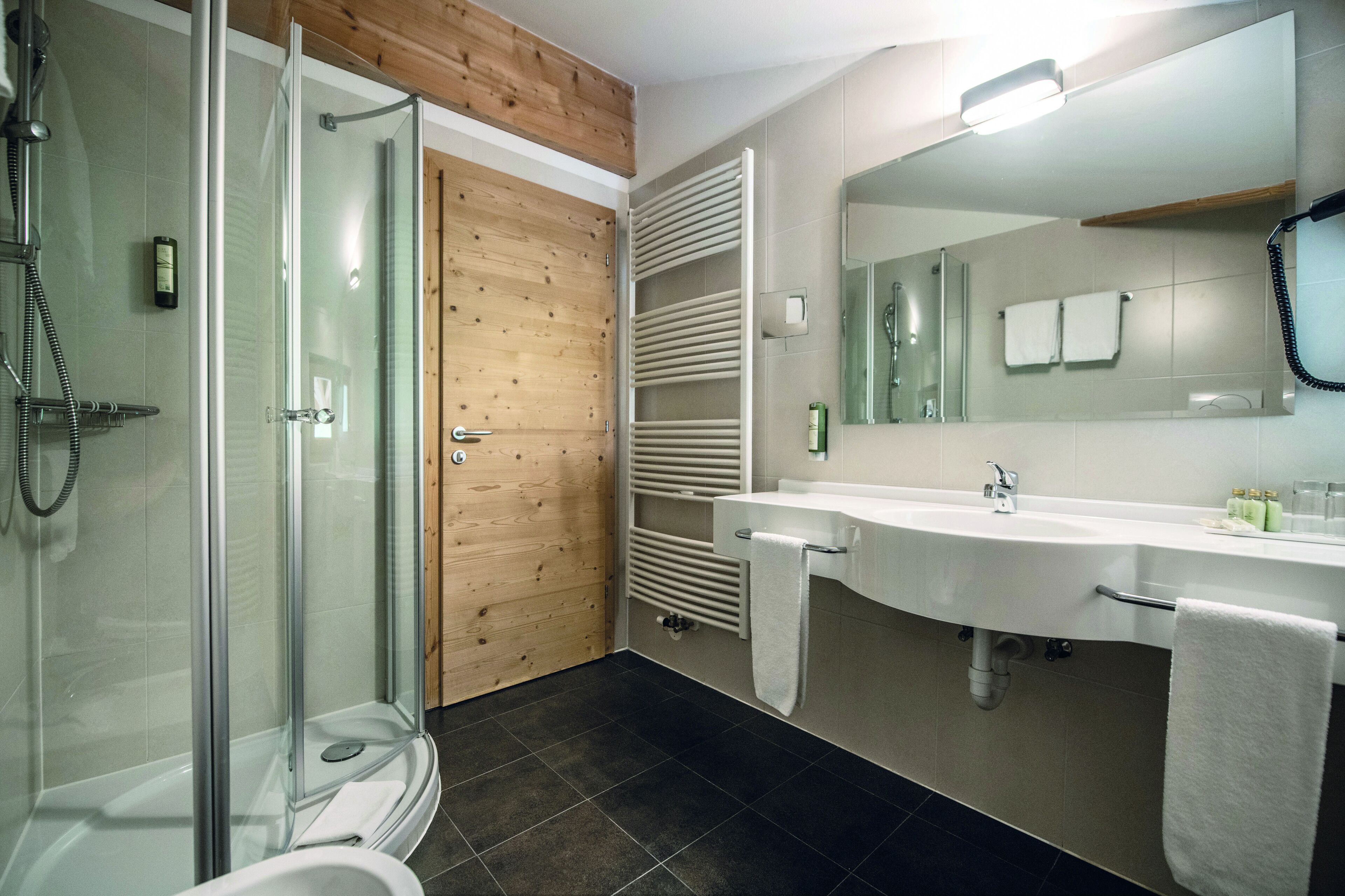 A modern bathroom with a glass shower enclosure, a wooden door, a white sink with a mirror, and a towel rack.
