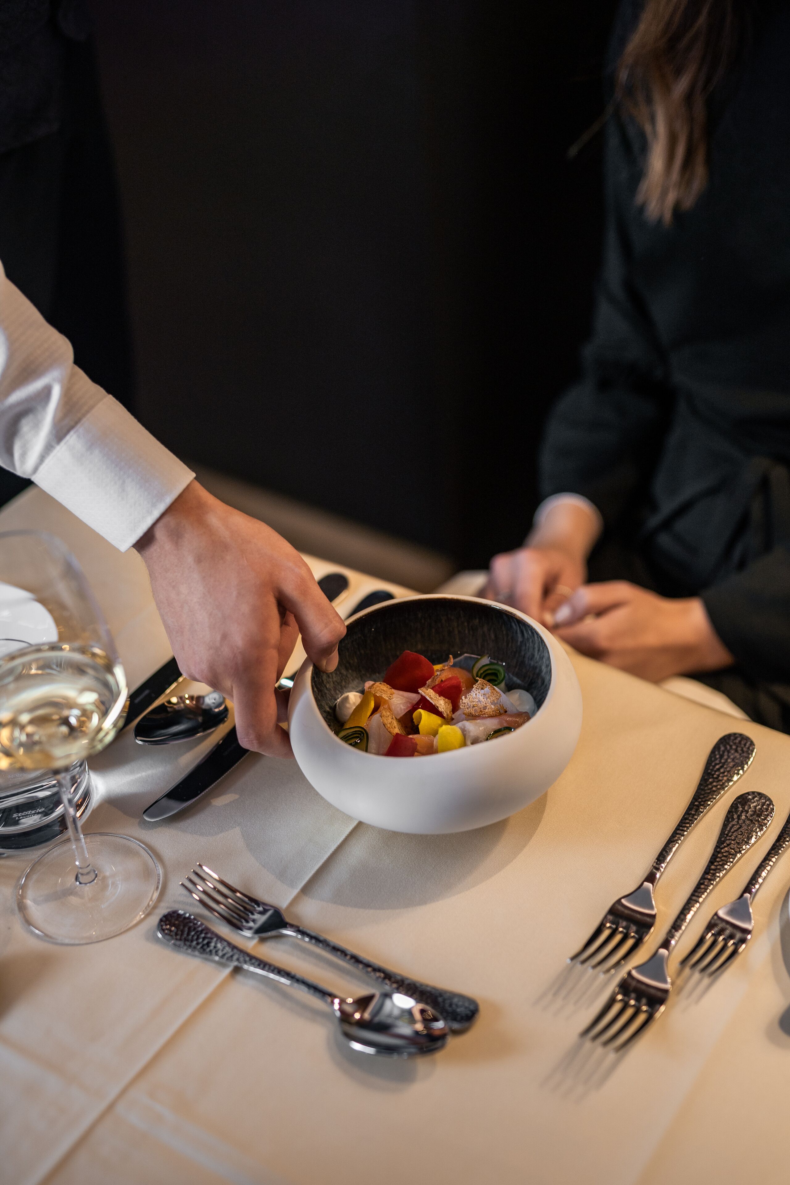 Ein Esstisch mit einer Schüssel Essen, Besteck und einem Weinglas.