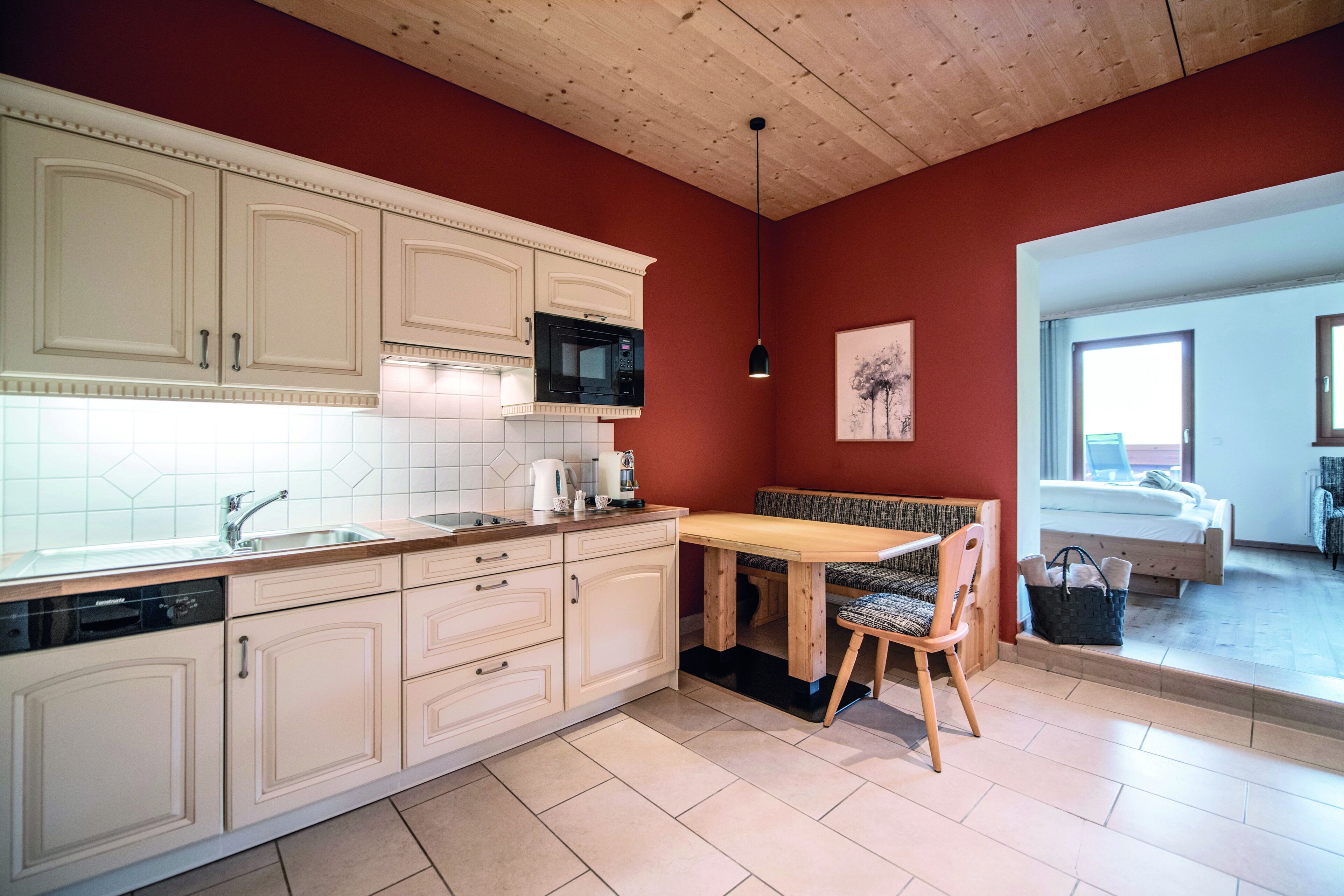 Une cuisine avec des meubles blancs, un four à micro-ondes et une table à manger en bois, accompagnée d’une chaise.