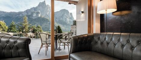 A room with a leather sofa, a dining table with chairs, and a view of mountains through a glass door.