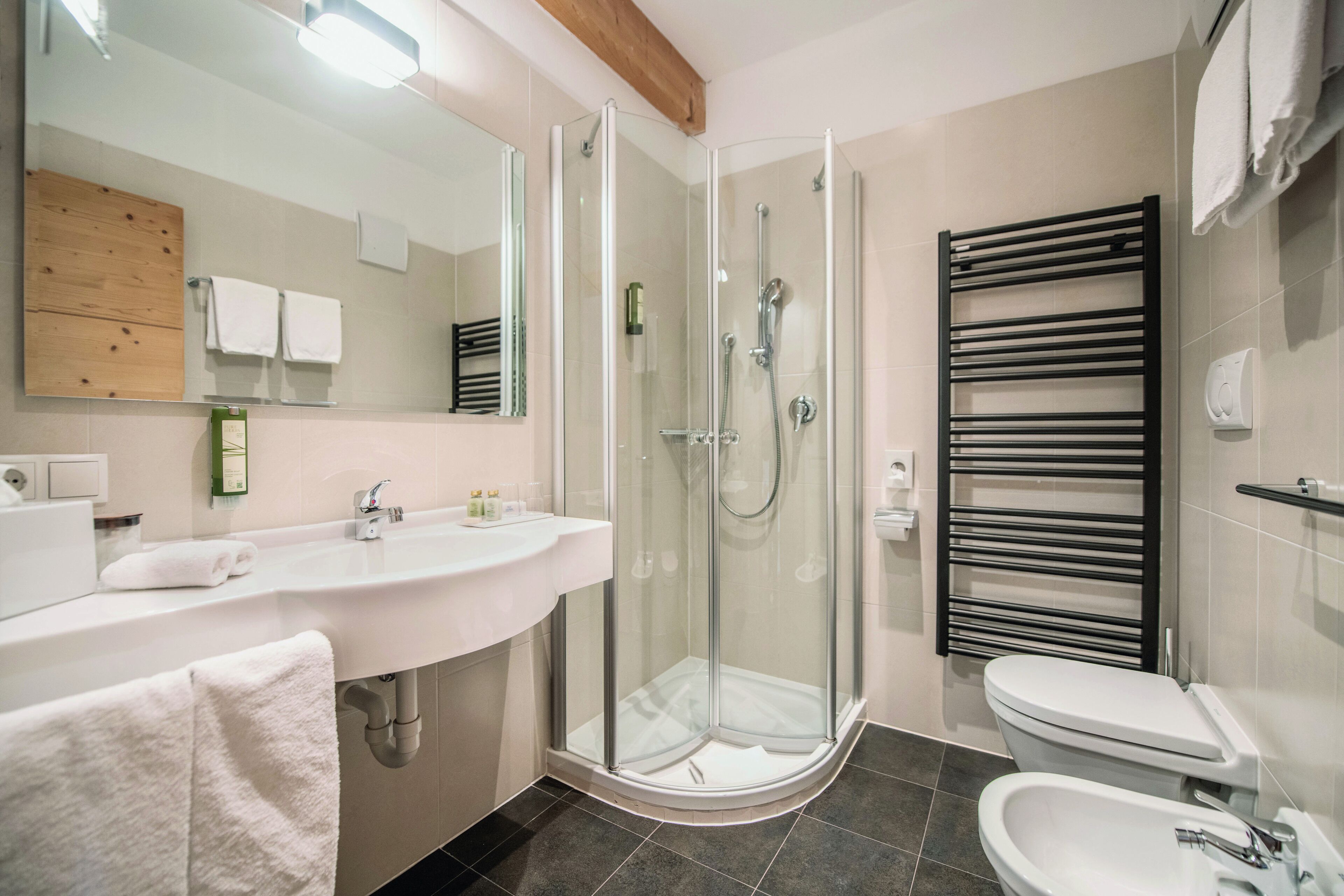 Un baño moderno con ducha de vidrio, un lavamanos blanco y un toallero negro.