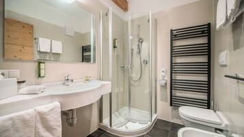 Un baño moderno con ducha de vidrio, un lavamanos blanco y un toallero negro.