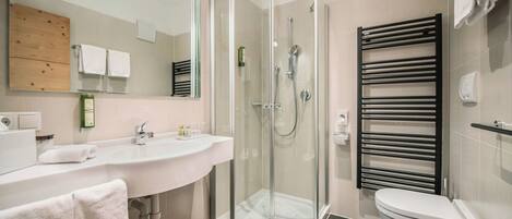 Un baño moderno con ducha de vidrio, un lavamanos blanco y un toallero negro.