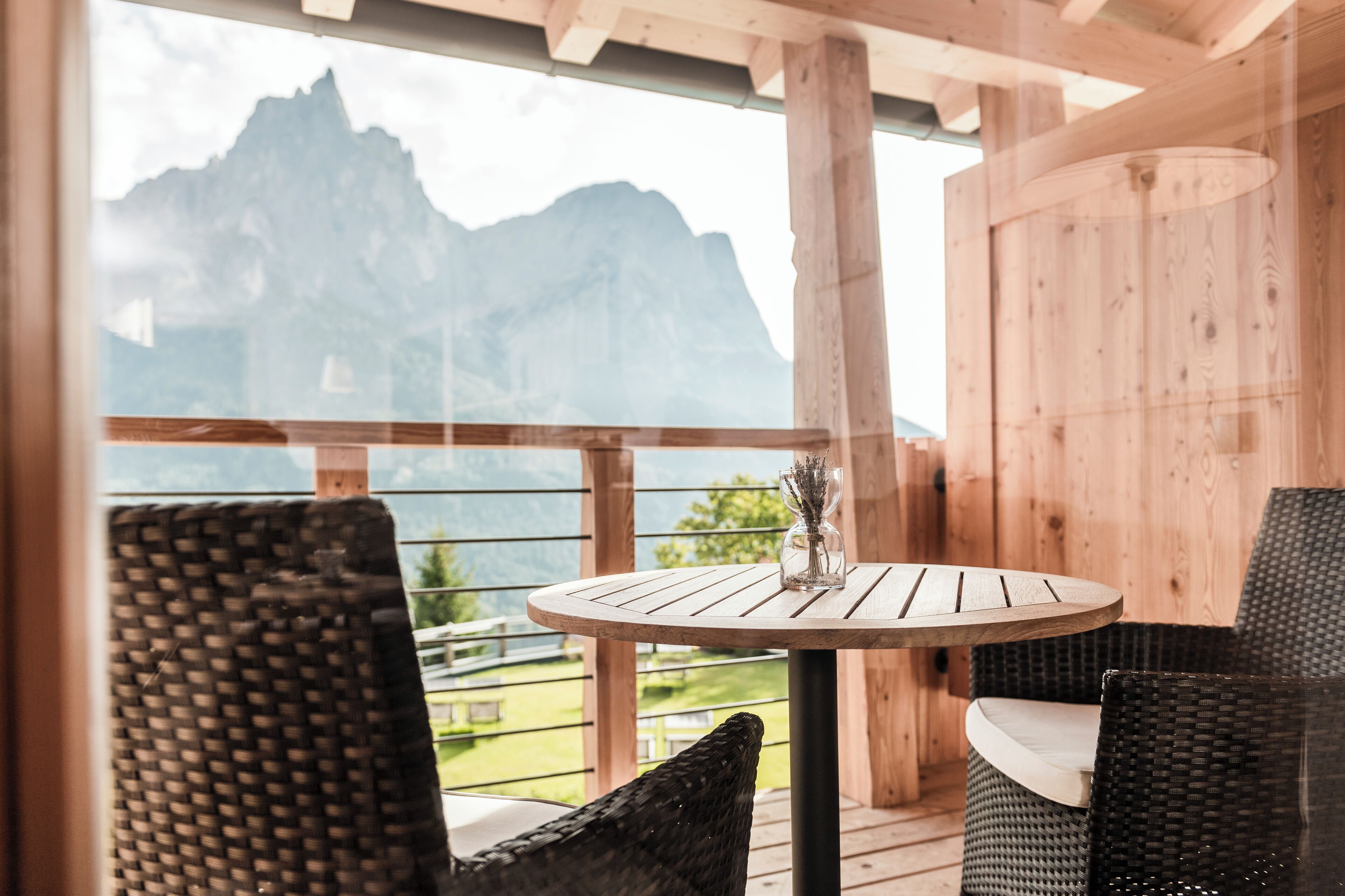 Une terrasse en bois avec une table ronde et des chaises en osier, offrant une vue sur un paysage montagneux.