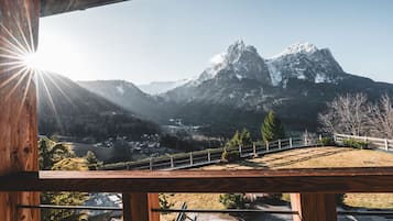 Une vue sur la montagne depuis un balcon en bois doté d’une balustrade, surplombant une vallée et des sommets enneigés.