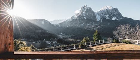 A mountain view from a wooden balcony with a railing, overlooking a valley and snow-capped peaks.