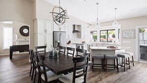 A spacious kitchen with a large island, dark wooden dining table, and modern pendant lights. - Pool, foosball, family fun at Always Summertime! (Scottsdale)