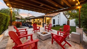 A covered outdoor patio with red Adirondack chairs, a fire pit, and string lights. - Pool, foosball, family fun at Always Summertime! (Scottsdale)