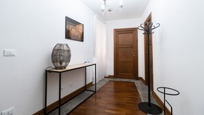 Un pasillo con suelo de madera, una consola con una lámpara decorativa, una puerta y un perchero.