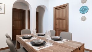Un comedor con una mesa de madera dispuesta para cuatro personas, rodeada de sillas. Hay dos puertas de madera y un plato decorativo colgado en la pared.