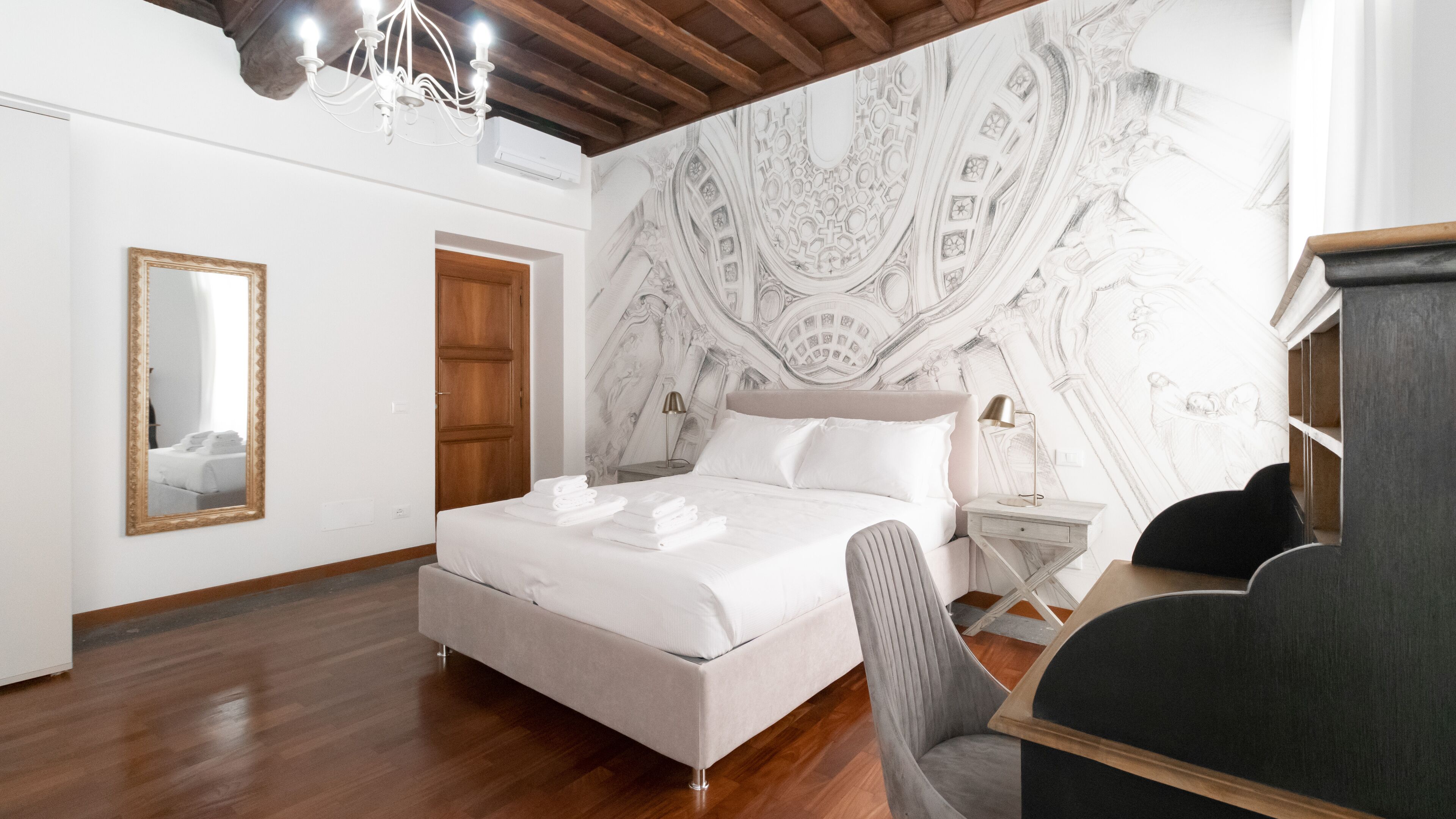 A modern hotel room with a large bed, a wooden floor, a mirror, and a wall with intricate architectural designs.