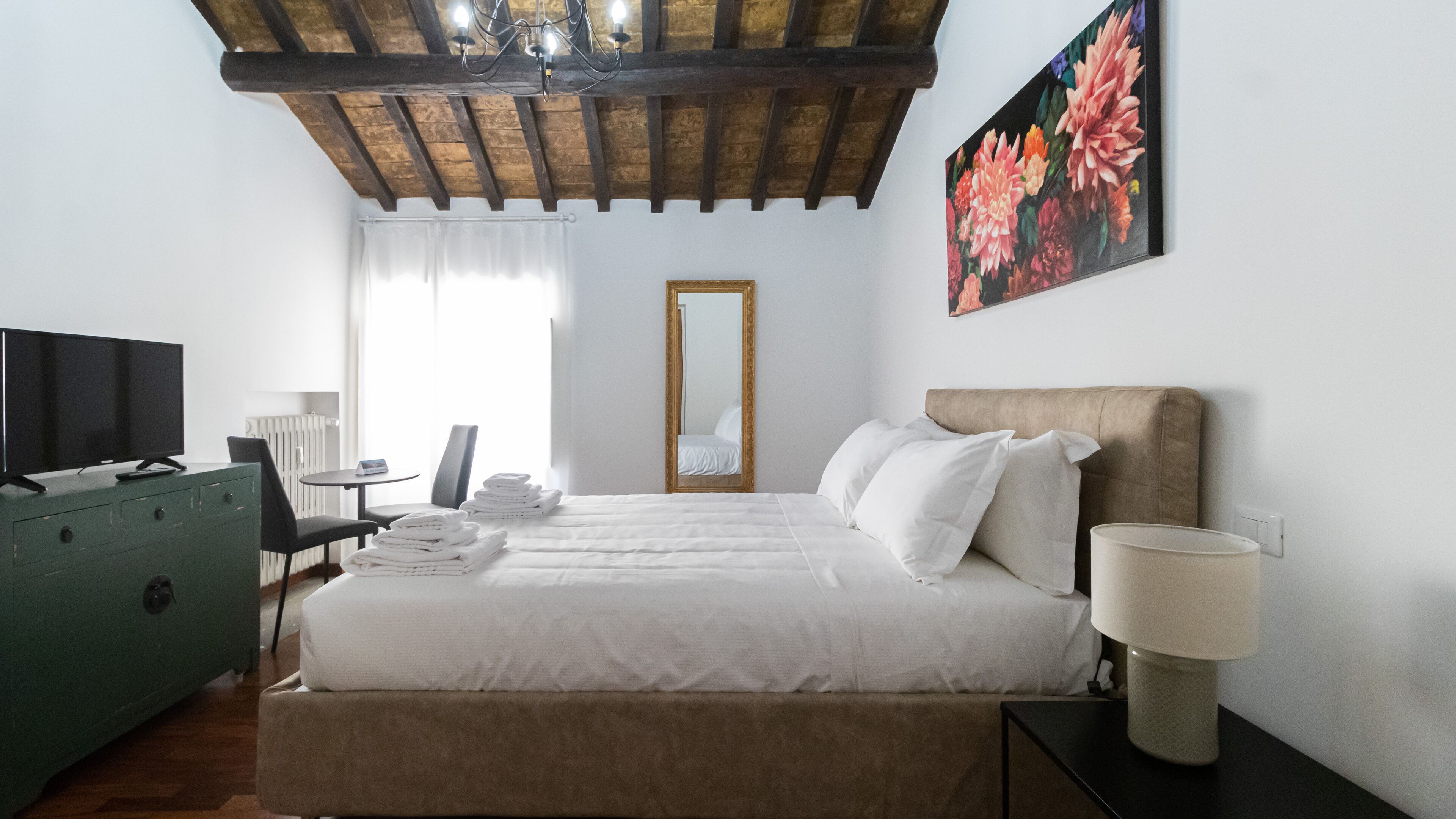 A hotel room with a bed, a TV, a dresser, a chair, and a painting on the wall.
