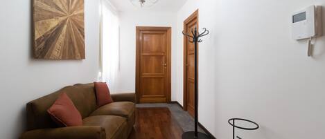 Un pasillo con una puerta de madera, un perchero, una mesita y un sofá con cojines.
