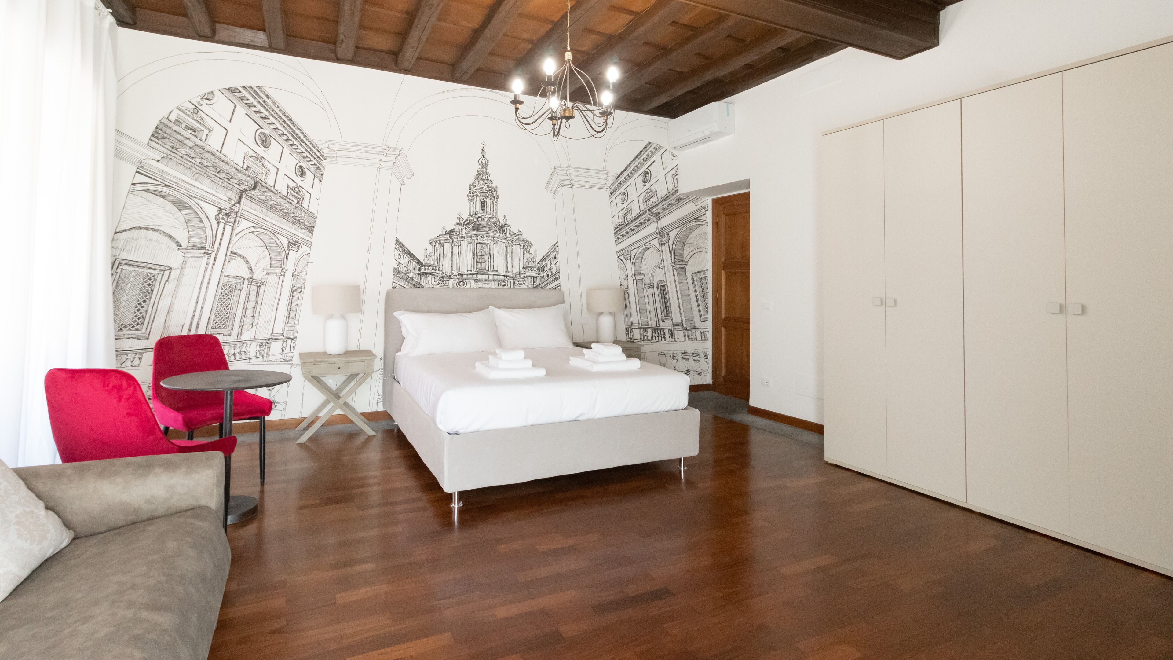 Un dormitorio con cama, una silla roja, una mesita y una araña.