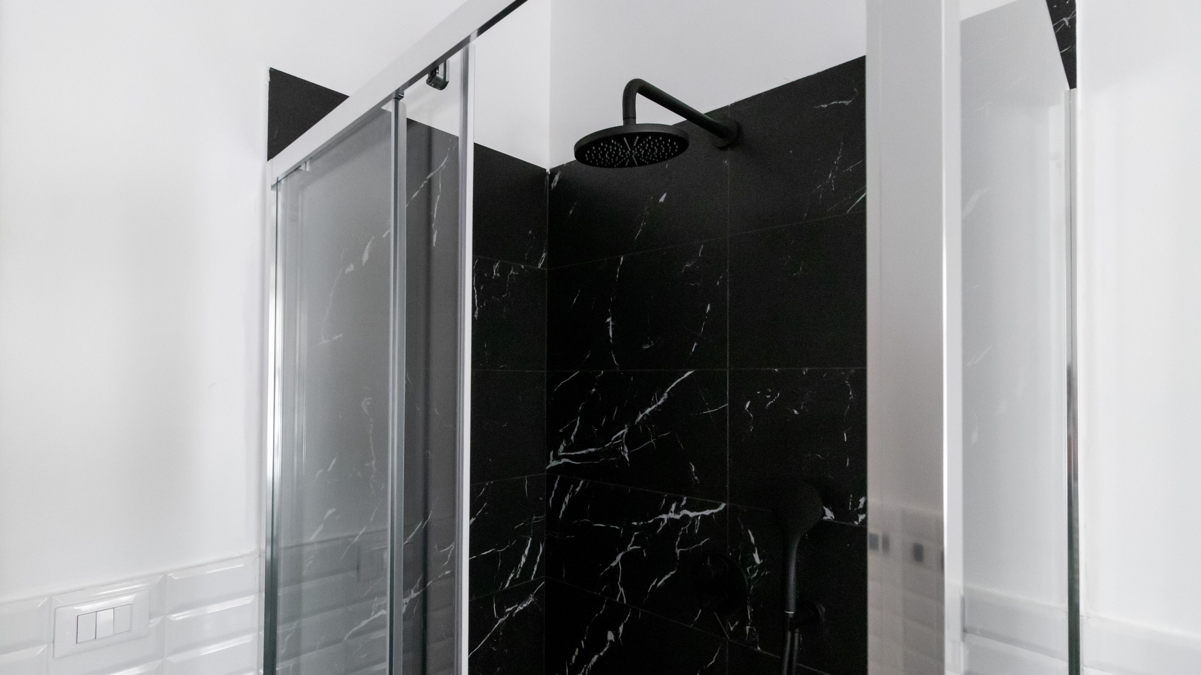 Un bagno moderno con box doccia in vetro, piastrelle in marmo nero e parete bianca.