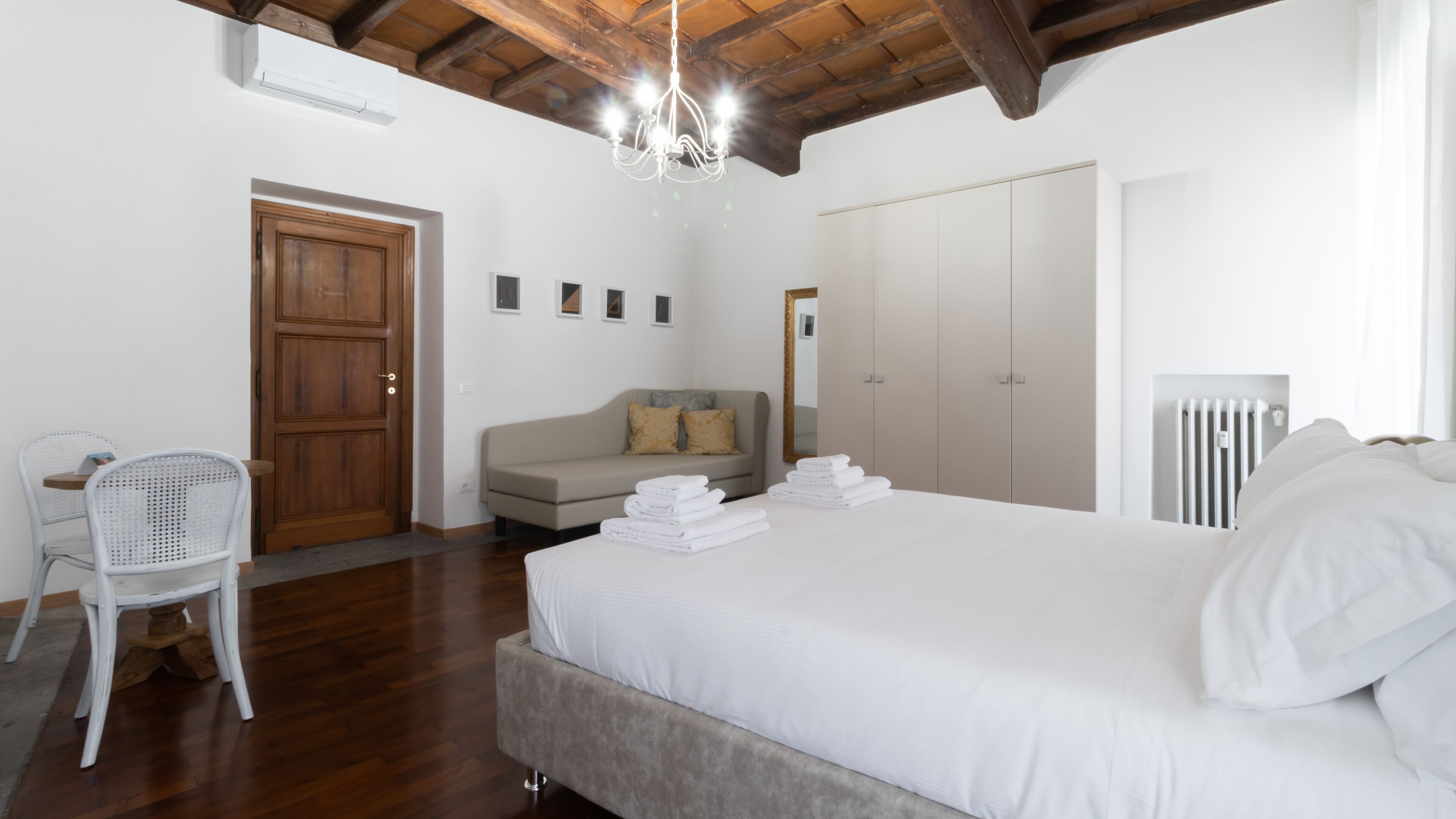 Quarto com cama grande, porta de madeira, sofá, cadeira e radiador.