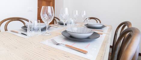 A dining table set with clear glassware, plates, and bowls, with a wooden chair and a door in the background.