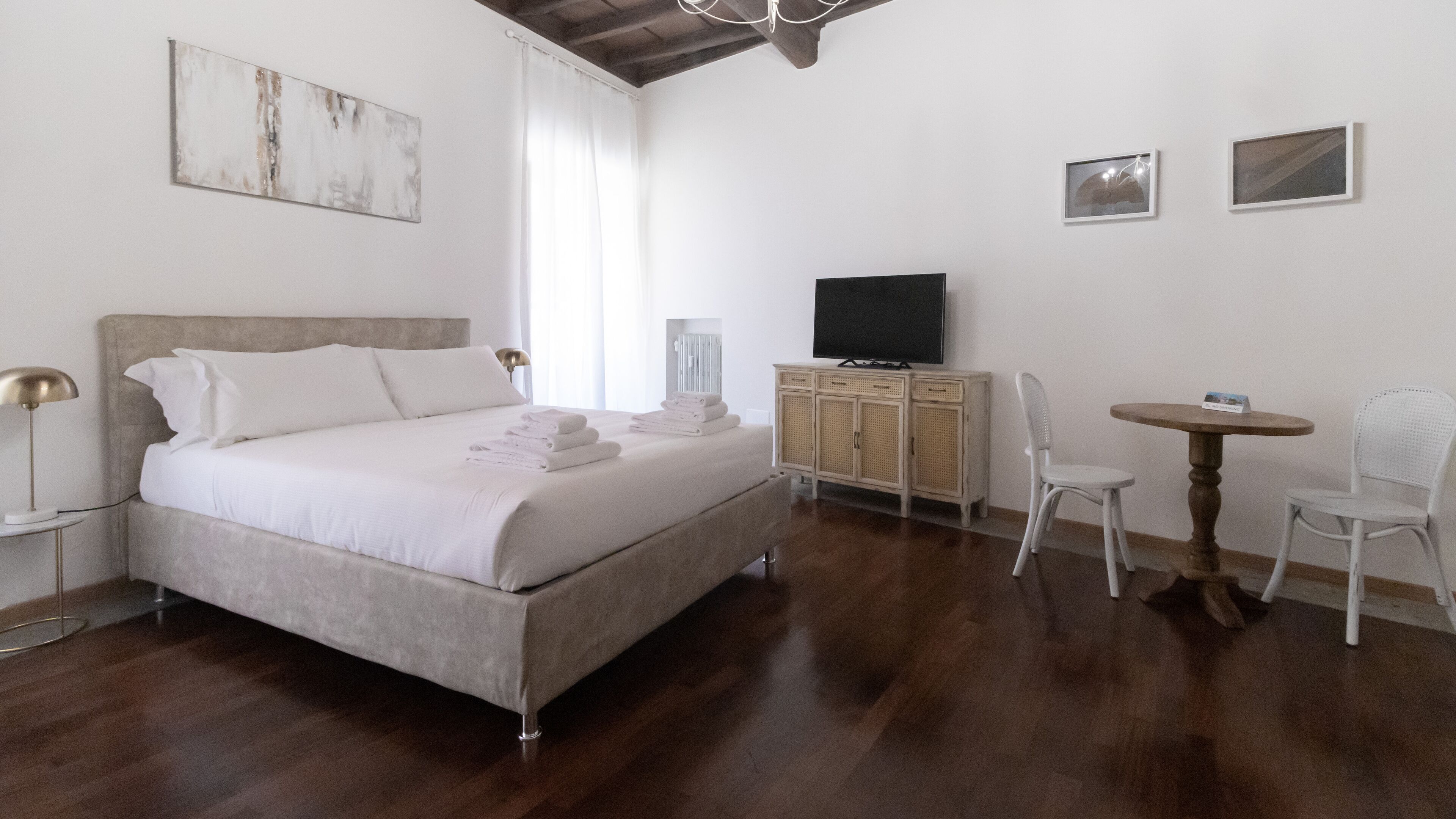A bedroom with a bed, a TV, a small table, and a chair.
