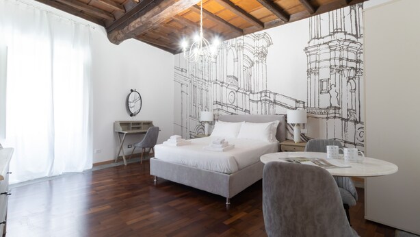 Una habitación de hotel moderna con una cama, un escritorio, una silla, una mesa redonda y una pared con dibujos arquitectónicos.