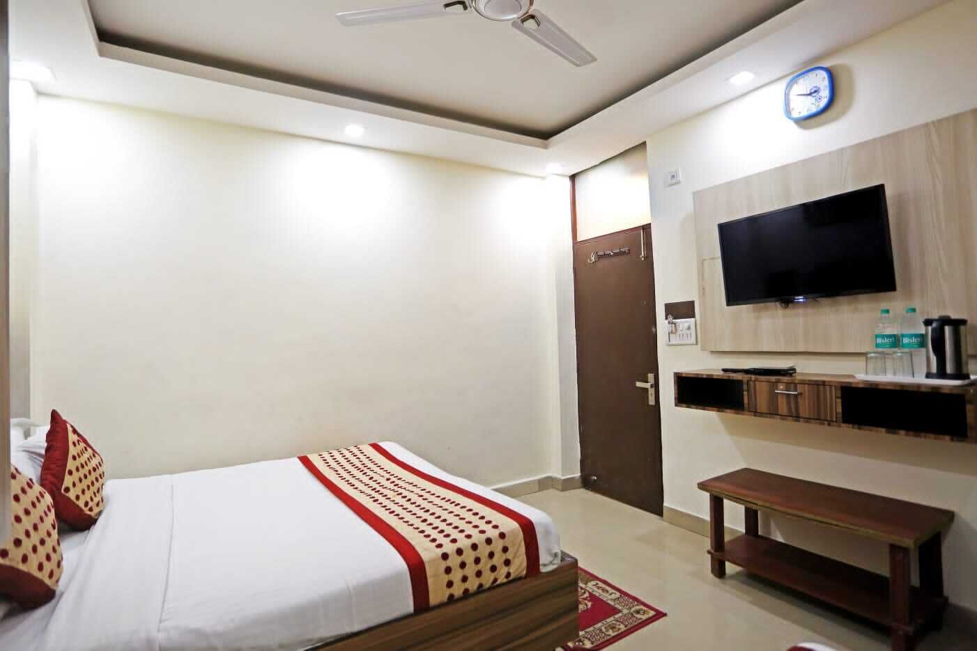 A hotel room with a bed, a TV, a wooden cabinet, and a clock on the wall.
