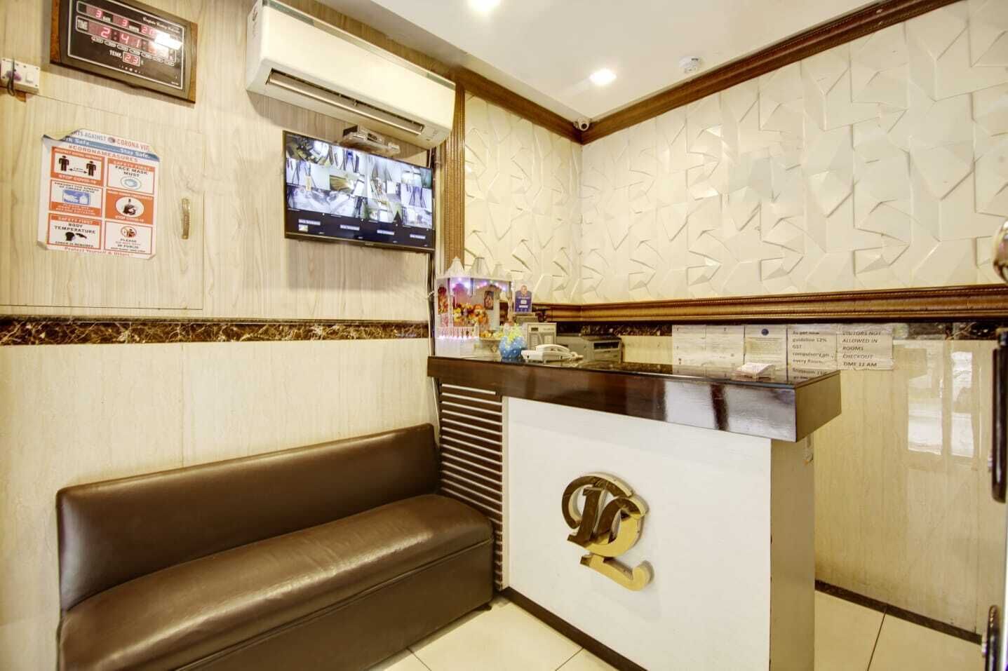 A reception area with a brown leather bench, a digital clock, a TV mounted on the wall, and a decorative wall panel.