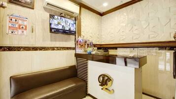A reception area with a brown leather bench, a digital clock, a TV mounted on the wall, and a decorative wall panel.
