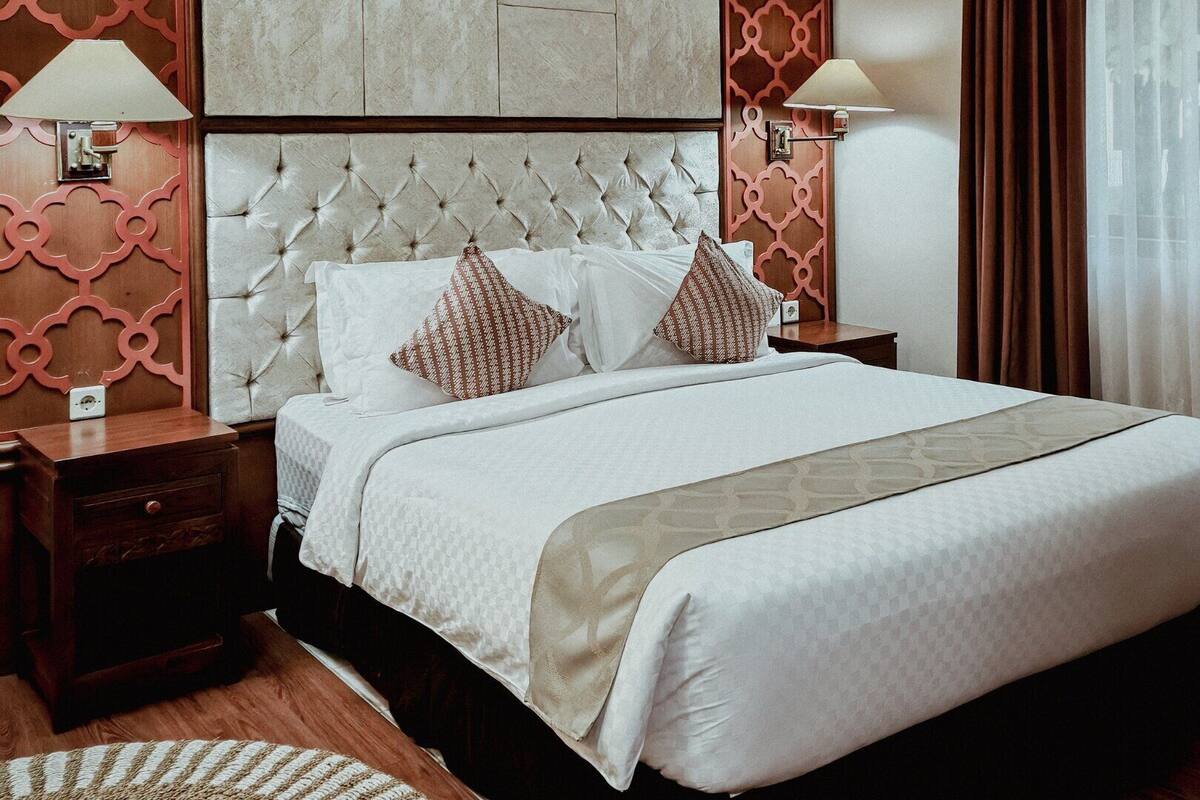 A neatly made bed with a tufted headboard, two bedside tables with lamps, and a patterned throw blanket.