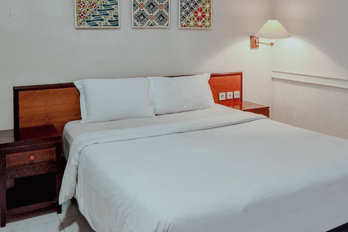 A neatly made bed in a hotel room with a wooden headboard, a nightstand, and a wall-mounted lamp.