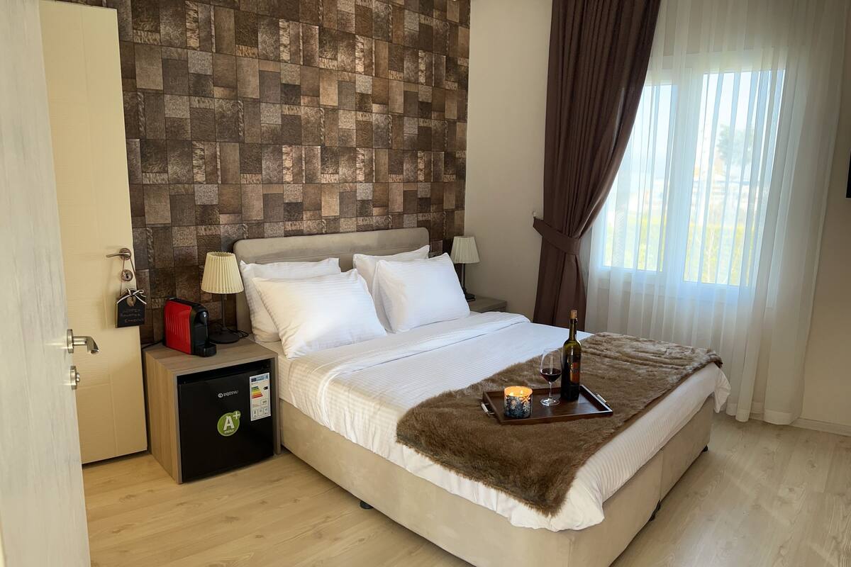 Une chambre d’hôtel avec un lit, une table de chevet avec une lampe, un minibar et une fenêtre avec des rideaux.