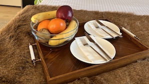Et hotelværelse med en seng, et natbord, en lampe, en kaffemaskine og et bakke med frugt og bestik.