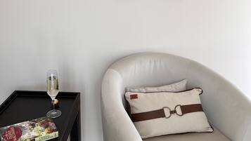 A room with a white armchair, a black side table with a glass of wine and a magazine, and a painting on the wall.
