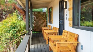 Een overdekt buitenterrein met houten banken en tafels, een houten omheining en uitzicht op groen.