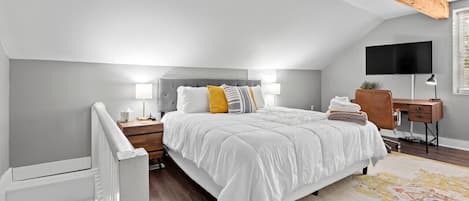 A bedroom with a bed, bedside tables, a desk, and a TV.