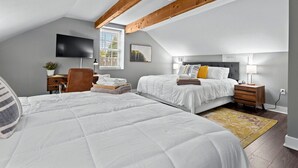 A bedroom with two beds, a TV, a desk, and a window. - Historic Main St. Customs House Upstairs Apartment (Saint Charles)