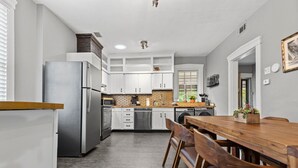 A modern kitchen with white cabinets, a stainless steel refrigerator, and a wooden dining table with chairs. - Historic Main St. Customs House Upstairs Apartment (Saint Charles)