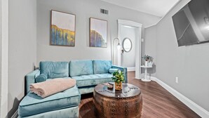 A living room with a blue sofa, a round coffee table with a plant, and artwork on the wall. - Historic Main St. Customs House Upstairs Apartment (Saint Charles)