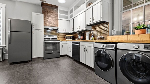 A modern kitchen with stainless steel appliances, white cabinetry, and a brick accent wall. - Historic Main St. Customs House Upstairs Apartment (Saint Charles)