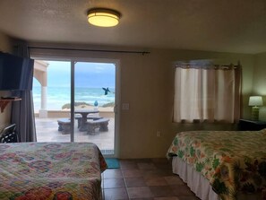 Een hotelkamer met twee bedden, een schuifdeur naar het strand en een plafondlamp.