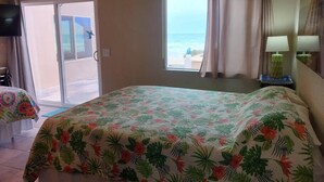 Habitació d'hotel amb llit, televisió, finestra que ofereix vistes a la platja i tauleta de nit amb làmpada.