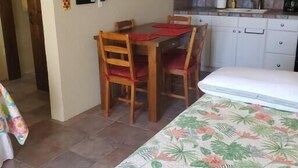 Habitació senzilla amb taula de dinar, cadires, llit, petita cuina i una porta que condueix a una altra habitació.
