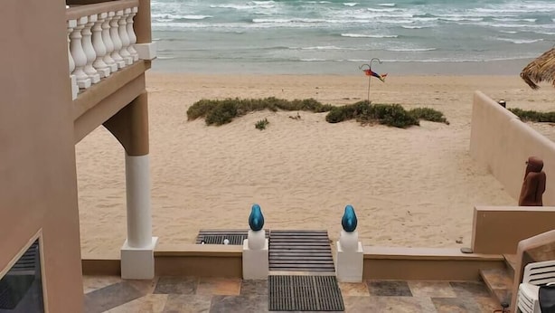 A beach view from a balcony with a railing, a small flag, and decorative vases. - Hacienda De Sol y Luna- 2 bdrm Apartment (Playa Encanto)