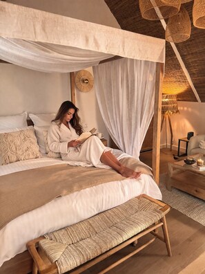 Une chambre à coucher avec un lit à baldaquin, une table de chevet avec une lampe, un banc et un objet décoratif fixé au mur.
