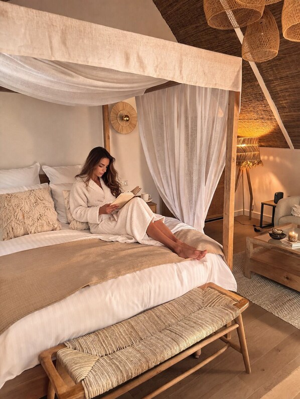 A bedroom with a canopy bed, a bedside table, a lamp, and a bench.