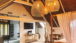Une pièce spacieuse avec un plafond haut, un lit, une table basse en verre avec une bougie, un bureau et une grande fenêtre.