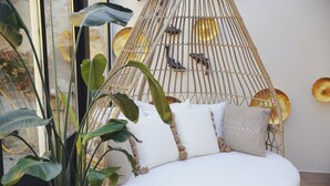 Une pièce avec un lit, un fauteuil suspendu et de grandes plantes vertes.