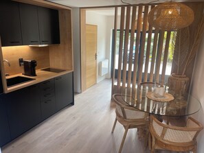 Una cucina moderna con una macchina per caffè, un tavolo da pranzo in legno con sedie e un vano divisorio in vetro con lampadario intrecciato.