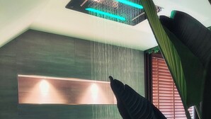 Une salle de bain moderne avec une baignoire, un luminaire fixé au mur et une fenêtre avec des stores.