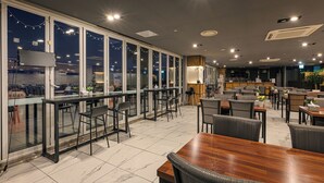 Un restaurant moderne doté d’un bar, de différents types de tables et de grandes fenêtres offrant une vue sur la ville.
