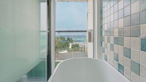 Une salle de bain avec une baignoire, une cabine de douche en verre et une vue sur l’océan et les bâtiments.