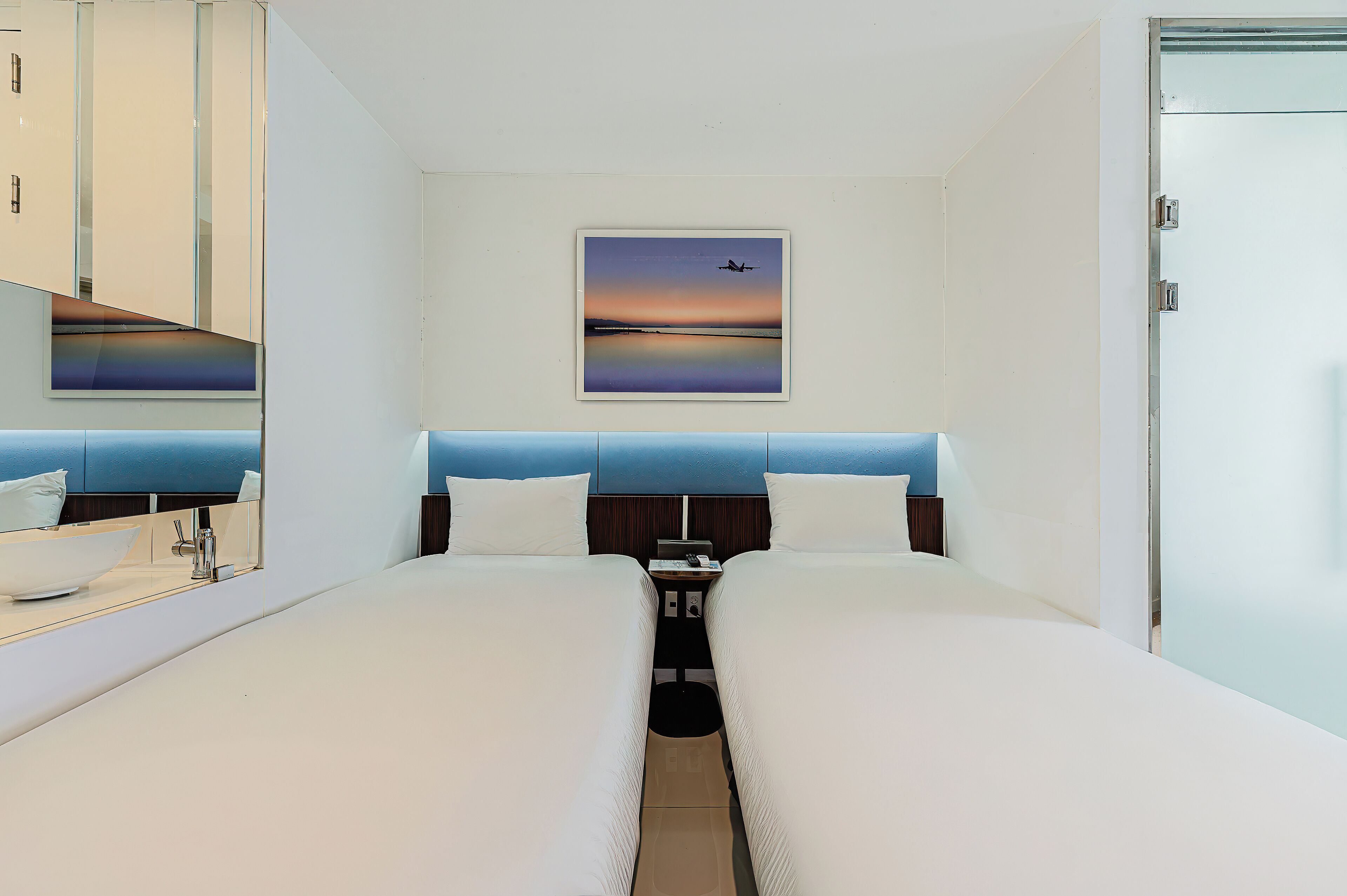A hotel room with two beds, a nightstand, a mirror, and a painting of a sunset.